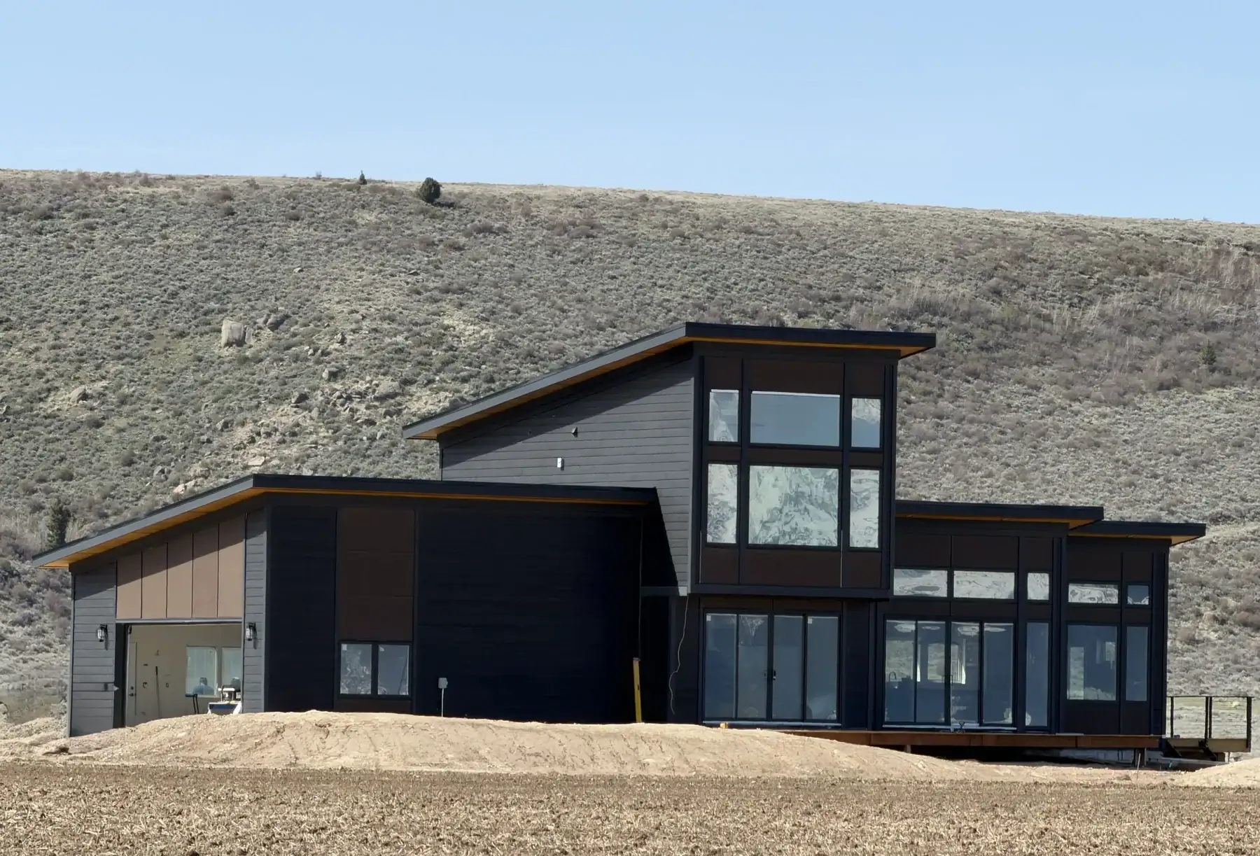 Fraisse - IMG_3149 Contemporary dark sided custom home with large windows and angled rooflines, set against a dry, shrub covered hillside in Idaho.
